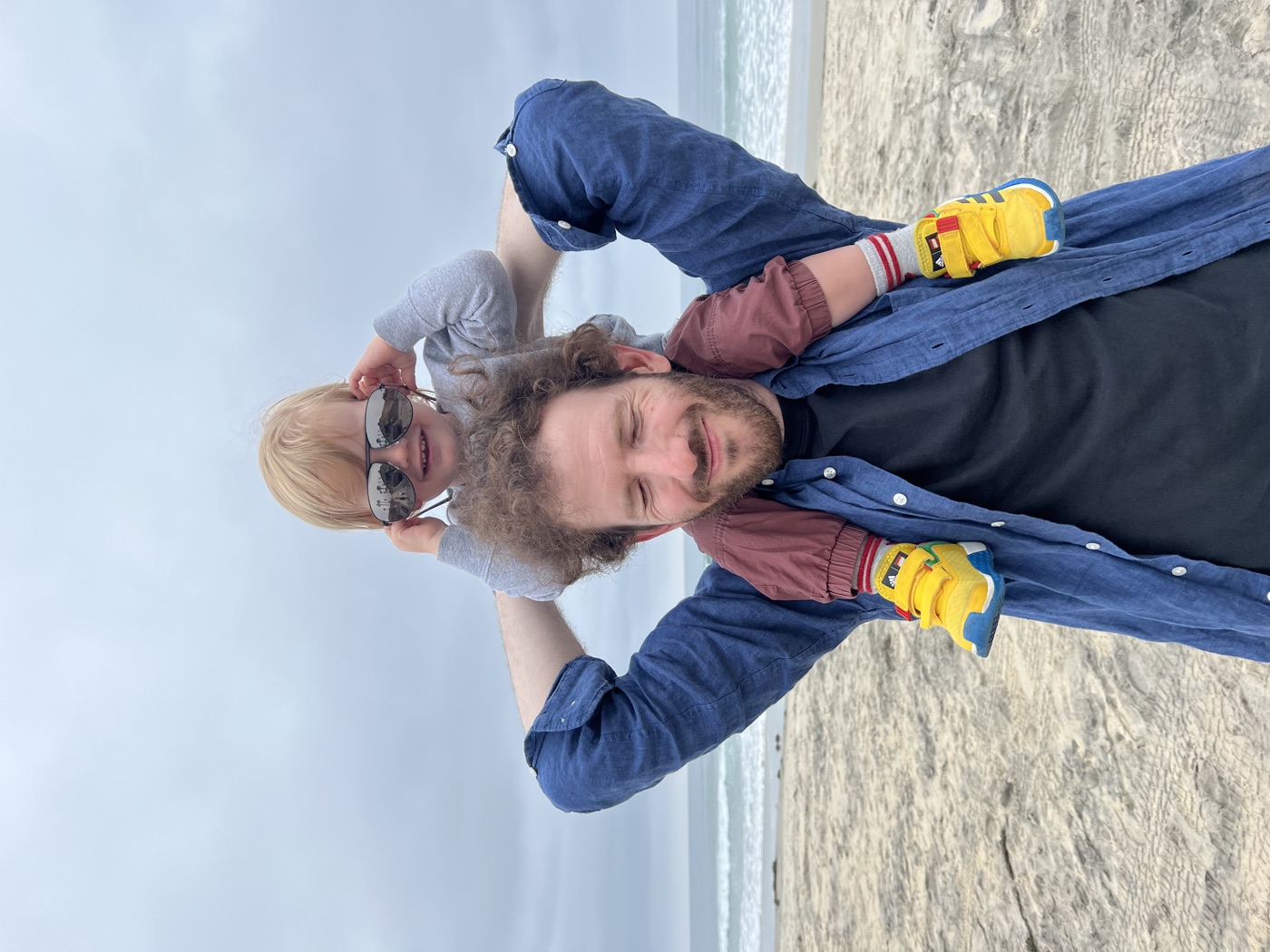 Jon Kantrowitz at the beach with a toddler in sunglasses riding on Jon's shoulders